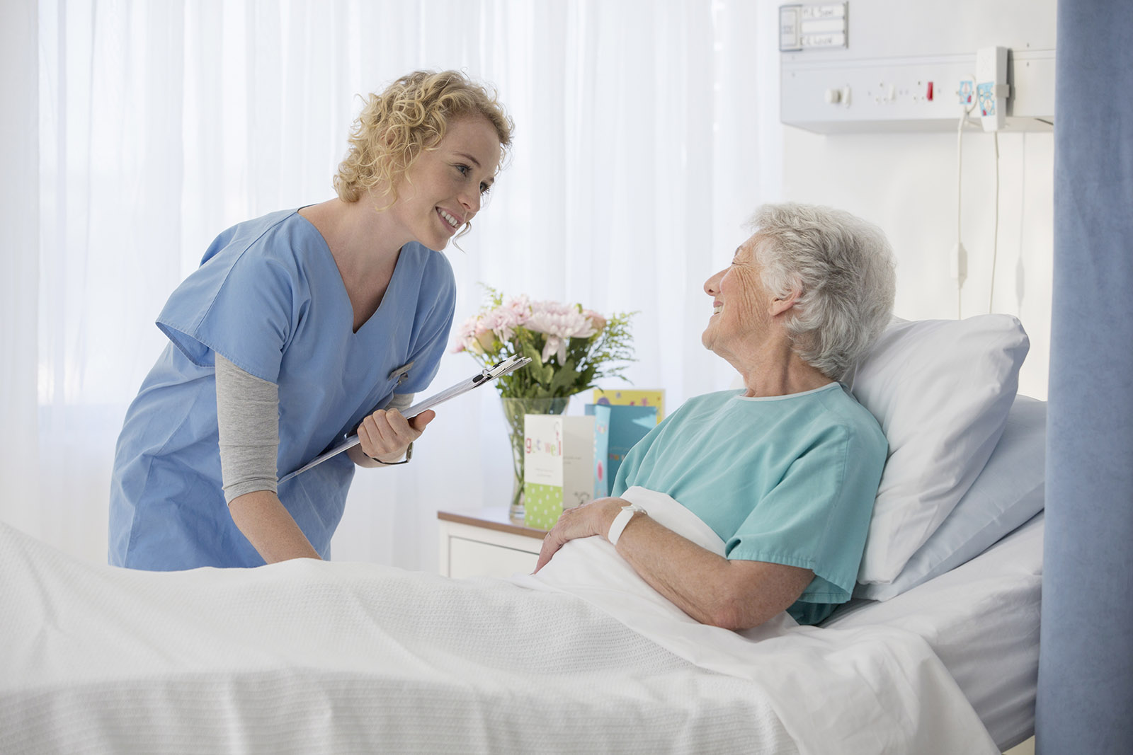 Kvinna lutar sig fram mot en äldre kvinna i en sjukvårdssäng