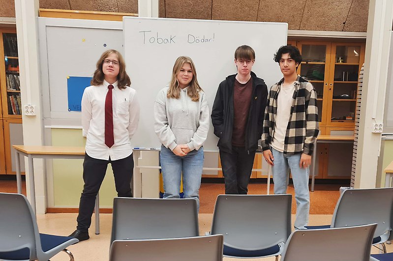 Fyra ungdomar står framför en whiteboard och tomma stolar.