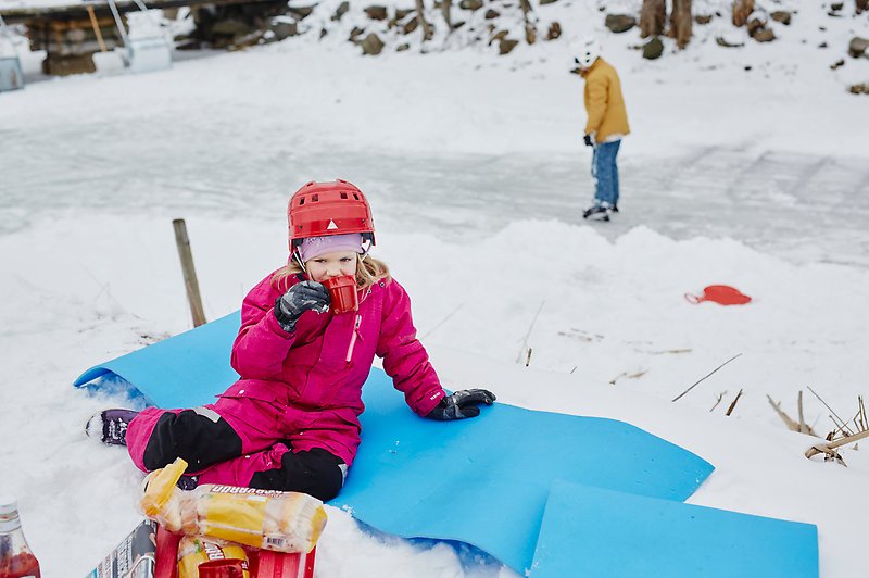 Ett barn sitter på en filt i snö och dricker.